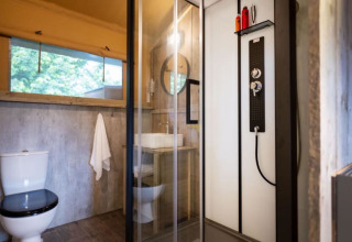 Baño en una tienda safari con ducha moderna, inodoro, lavabo, detalles de madera y ventana grande.