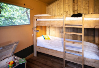Acogedor dormitorio con literas de madera en una tienda safari, ventana grande y vistas al verde exterior.