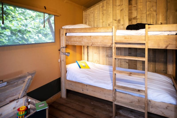 Acogedor dormitorio con literas de madera en una tienda safari, ventana grande y vistas al verde exterior.