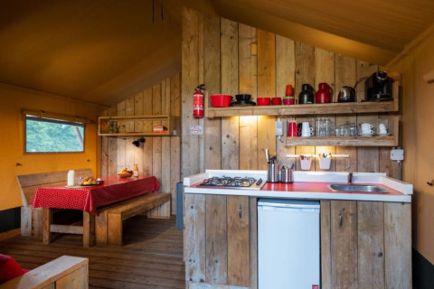Interior de tienda safari con cocina de madera, mesa de comedor y detalles en rojo bajo luz cálida.