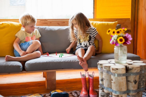 Two children playing a board game on a sofa inside a Barntent safari tent with flowers on a table.