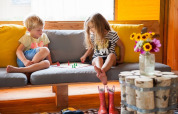 Dos niños juegan a un juego de mesa en un sofá dentro de una tienda safari Barntent, con flores cerca.