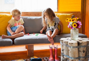 Two children playing a board game on a sofa inside a Barntent safari tent with flowers on a table.