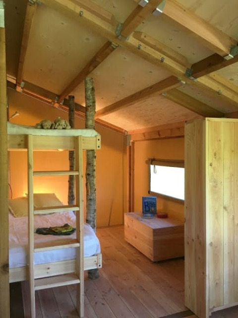 Intérieur d’une tente safari avec lits superposés et troncs d’arbres chez FarmCamps BoeBaDoe, Pays-Bas.