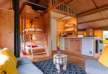 Interieur van een safaritent met houten meubels, keuken, stapelbedden en een knusse zithoek.