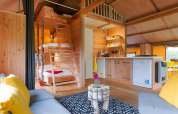 Vista interior de una tienda safari con muebles de madera, cocina, camas en altillo y zona de estar acogedora.