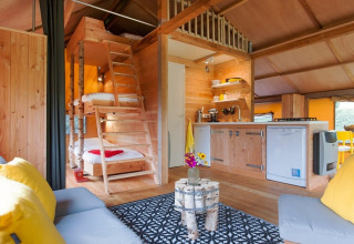 Interno di una tenda safari con arredi in legno, cucina, letti a soppalco e zona lounge accogliente.