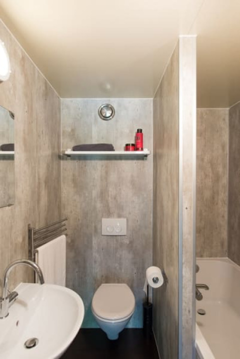 Photo of a compact safari tent bathroom with toilet, sink, shelf above, towel rail and bathtub.
