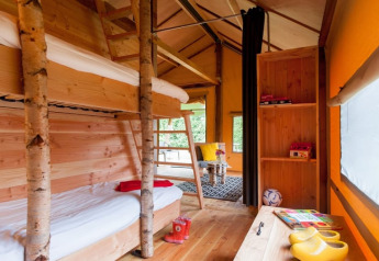 Intérieur de tente safari avec lits superposés, décor en bois, coin salon confortable et lumière naturelle.