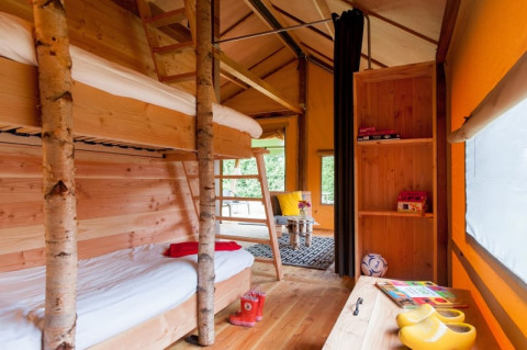 Interieur van een safaritent met stapelbedden, houten accenten, zithoek en overvloedig daglicht.