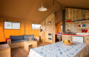 Innenraum eines Safarizeltes mit Holzmöbeln, gemütlichem Sofa, Esstisch und kleiner Küchenzeile.