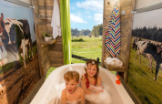 Twee kinderen genieten van een bad in een safaritent met koeiendecor en uitzicht op een weide met koeien.