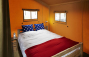 Interior de tienda safari con cama doble, cojines azules de lunares y aire acondicionado.