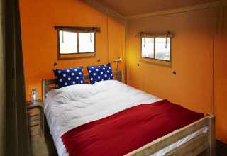 Interior de tienda safari con cama doble, cojines azules de lunares y aire acondicionado.