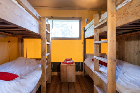 Interior view of a safari tent with two wooden bunk beds, yellow walls, a window, and simple decor.