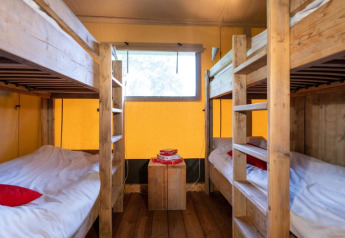 Interior view of a safari tent with two wooden bunk beds, yellow walls, a window, and simple decor.