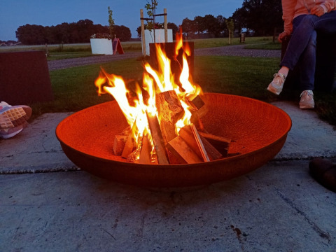 Hoguera en un gran cuenco de fuego con personas alrededor en Boerderijcamping het Katreel, Overijssel, Países Bajos.