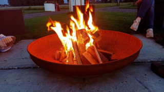 Hoguera en un gran cuenco de fuego con personas alrededor en Boerderijcamping het Katreel, Overijssel, Países Bajos.