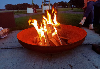 Hoguera en un gran cuenco de fuego con personas alrededor en Boerderijcamping het Katreel, Overijssel, Países Bajos.