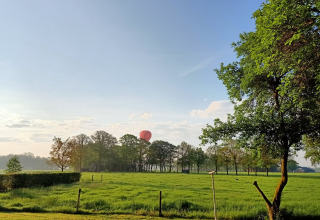 Grüne Wiese, Bäume und ein roter Heißluftballon bei Boerderijcamping het Katreel in Overijssel, Niederlande.