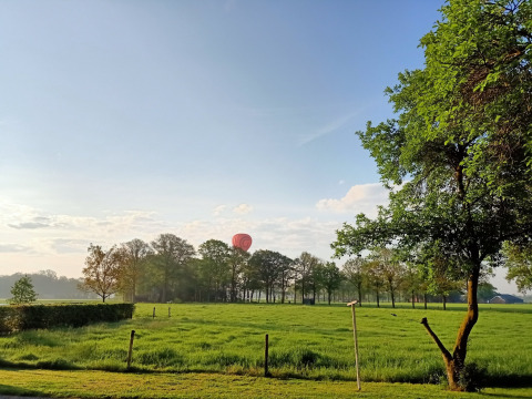 Campo verde, árboles y un globo aerostático rojo en Boerderijcamping het Katreel, Overijssel, Países Bajos.
