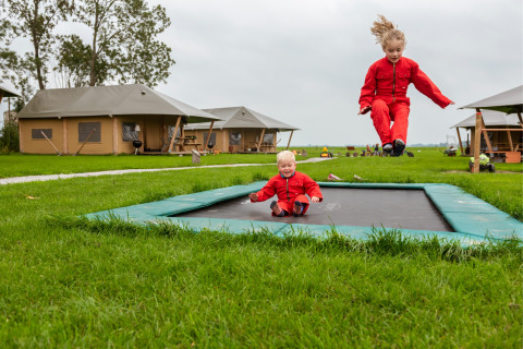 Deux enfants en rouge jouent sur un trampoline à FarmCamps Kooij Hoeve, parc de vacances en Hollande-Méridionale.