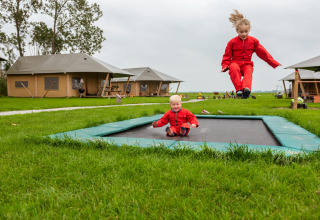 To børn i rødt leger på en trampolin foran glampingtelte hos FarmCamps Kooij Hoeve i Sydholland.