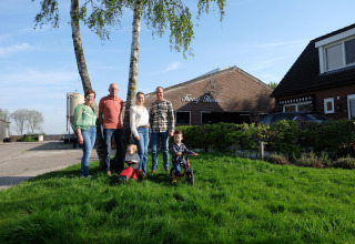 En familie står foran FarmCamps Kooij Hoeve feriepark i Sydholland, Holland, med børn på græsset.