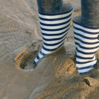Persona con botas de lluvia a rayas azules y blancas sobre lodo en parque vacacional con glamping.