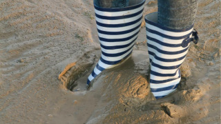 Persona con botas de lluvia a rayas azules y blancas sobre lodo en parque vacacional con glamping.