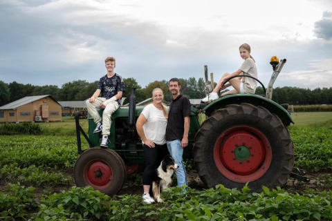 Family and dog pose by a tractor in a field at a Limburg, Netherlands holiday park with cabins nearby.