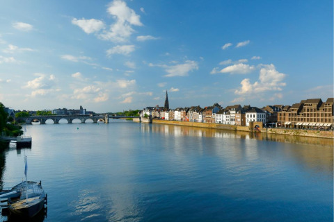 Vista panorámica de un río, puente antiguo y edificios históricos junto a un parque vacacional con glamping.