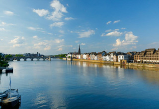 Panoramabillede af en flod, historisk bro og gamle bygninger ved en feriepark, hvor der tilbydes glamping.