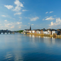 Vista panorámica de un río, puente antiguo y edificios históricos junto a un parque vacacional con glamping.