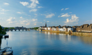 Panoramabillede af en flod, historisk bro og gamle bygninger ved en feriepark, hvor der tilbydes glamping.