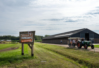Welkomstbord van FarmCamps De Kalverliefde met tractor en bezoekers bij een grote schuur in Limburg.