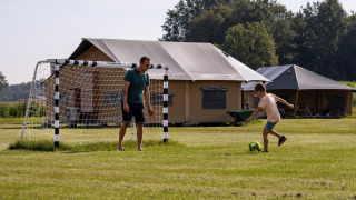 Een man en een kind spelen voetbal voor safaritenten op FarmCamps De Kalverliefde in Limburg, Nederland.