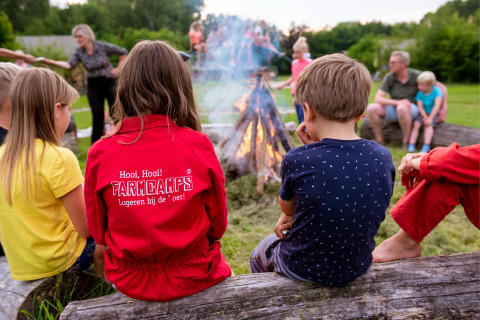 Børn og voksne sidder omkring et lejrbål på FarmCamps Den Branderhorst i Gelderland, Holland.