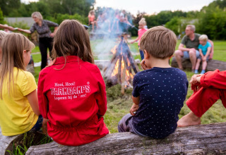 Børn og voksne sidder omkring et lejrbål på FarmCamps Den Branderhorst i Gelderland, Holland.