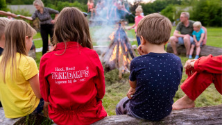Niños y adultos sentados alrededor de una fogata en FarmCamps Den Branderhorst, Gelderland, Países Bajos.