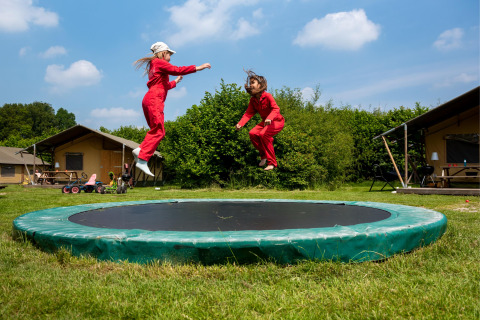 Twee kinderen in een rode overall springen op een trampoline bij FarmCamps Den Branderhorst in Gelderland.