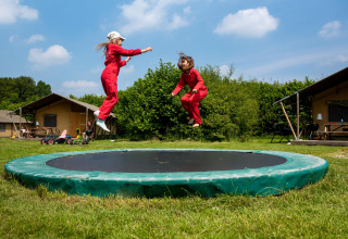 To børn i røde dragter hopper på en trampolin i et grønt område på FarmCamps Den Branderhorst.
