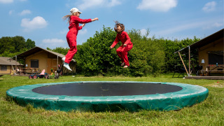 Dos niños con monos rojos saltan en una cama elástica en FarmCamps Den Branderhorst, Gelderland.