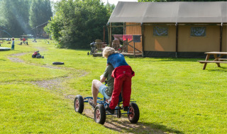 Niños jugando y montando un kart en FarmCamps Den Branderhorst, un parque vacacional en Gelderland, Países Bajos.