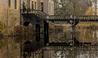 Foto de un edificio histórico con un puente sobre un estanque, rodeado de árboles en un parque vacacional.