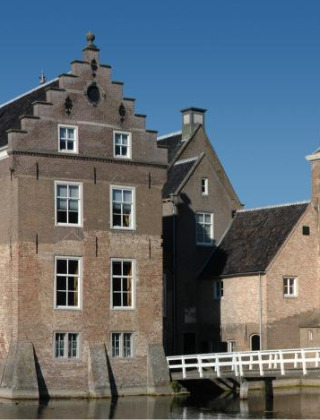 Castillo histórico junto a un foso y puente blanco, rodeado de árboles cerca de Hengelo, Gelderland, Países Bajos.