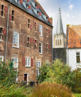 Edificio de ladrillo y torre de iglesia junto a un jardín cerca de Hengelo, Güeldres, Países Bajos, día soleado.