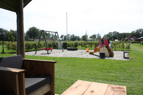 Blick von der Terrasse auf einen Spielplatz mit Schaukel und Rutsche auf dem Farm Campsite het Katreel.