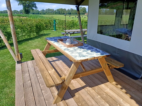 Mesa y banco de madera en terraza en una tienda safari en Farm Campsite de Katreel, Países Bajos, día soleado.