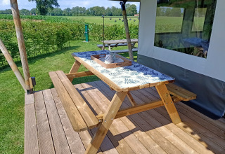 Træbord og bænk på terrasse ved safaritelte på Farm Campsite de Katreel i Holland, solrig dag.